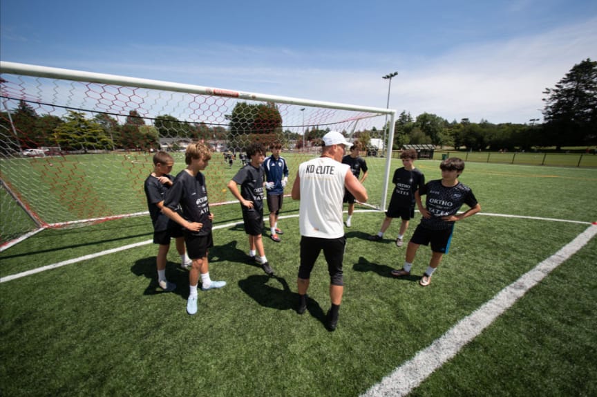 Kyle Degelman coaching a huddle of youth soccer players at a KD Elite camp in Victoria, BC